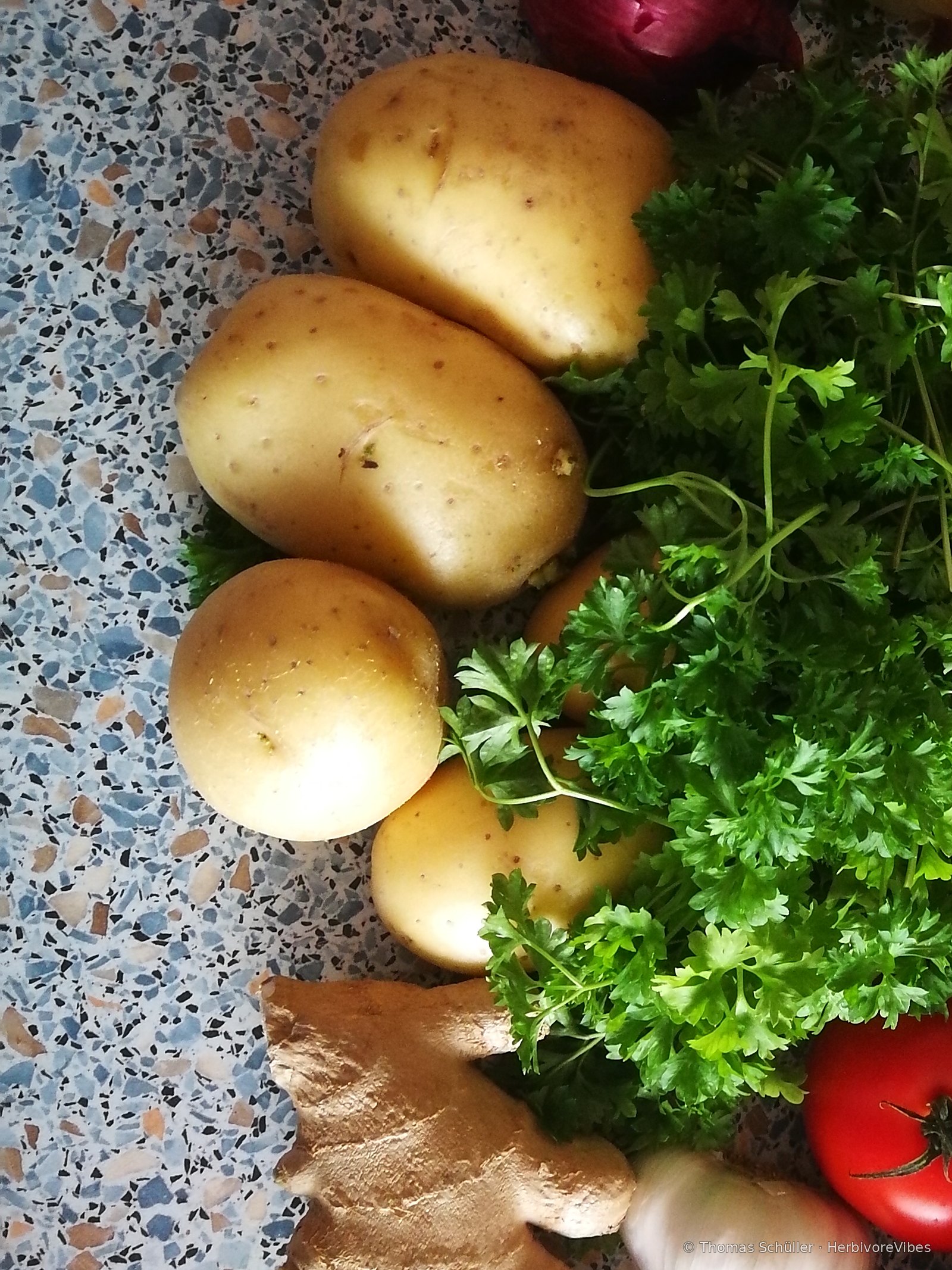 Erdäpfel, Petersilie, Ingwer, Knoblauch und eine Tomate auf einer Arbeitsplatte